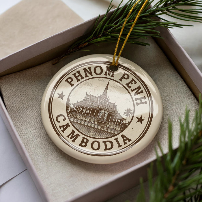 A decorative ornament with the text "PHNOM PENH" and "CAMBODIA" printed on it, surrounded by a decorative border and a sprig of pine branches.