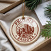 A decorative ornament with the text "PHOENIX ARIZONA" printed on it, hanging from a string. The ornament is placed on a white surface, with some greenery visible in the background.