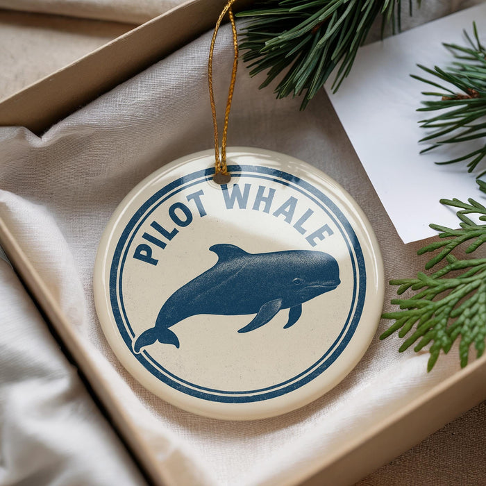 A round ornament with a blue whale image and the text "PILOT WHALE" is displayed in a box with pine branches.