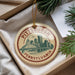 A circular ornament with the text "PITTSBURGH PENNSYLVANIA" and an illustration of a bridge and skyline, hanging from a string.