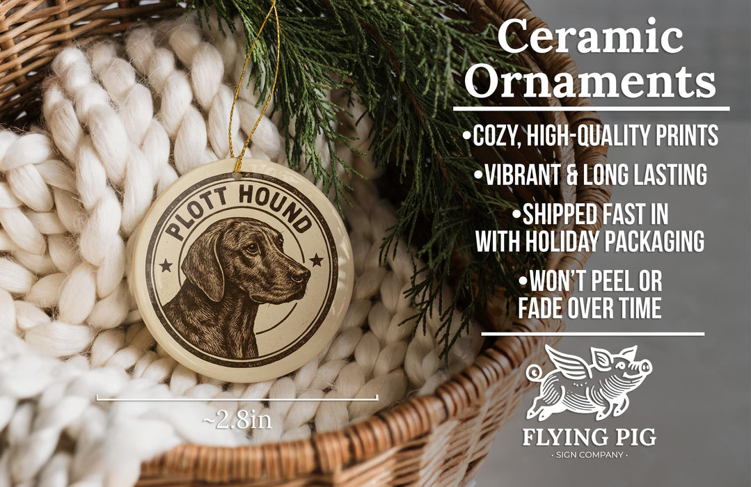 Ceramic ornaments, featuring a ceramic ornament with a dog's head and the text "PLOTT HOUND" and "FLYING PIG" printed on it, hanging in a basket with pine branches.