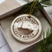 A circular ornament with the text "PORT ELIZABETH SOUTH AFRICA" printed on it, placed inside a box with pine branches.