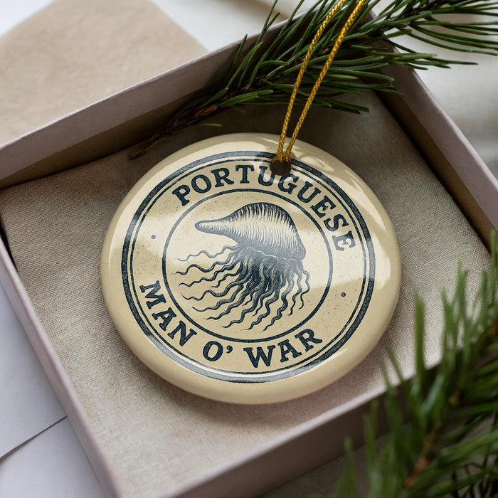 A circular ornament with the text "PORTUGUESE MAN O' WAR" printed on it, surrounded by a pine branch and pine needles.