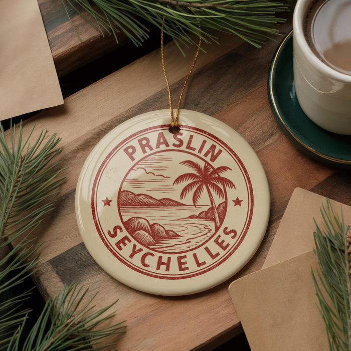 A circular ornament with the text "PRASLIN SEYCHELLES" is displayed on a wooden surface, surrounded by pine branches and a cup of coffee.
