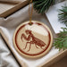 A circular ornament with a mantis illustration on it, hanging from a string.