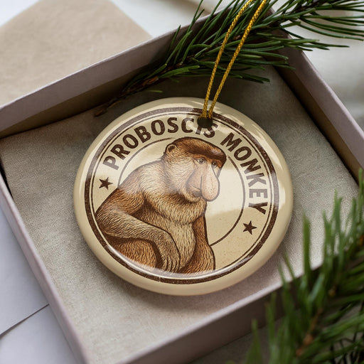 A round ornament featuring a monkey, with the text "PROBOSCIIS MONKEY" printed on it, is displayed in a box surrounded by pine branches.