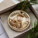 A round ornament featuring a monkey, with the text "PROBOSCIIS MONKEY" printed on it, is displayed in a box surrounded by pine branches.