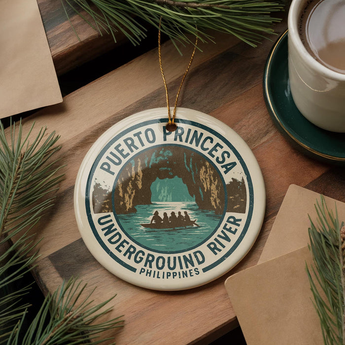 A round ornament with the text "PUERTO PRINCESA UNDERGROUND RIVER PHILIPPINES" and an illustration of a boat on a river, surrounded by pine branches and a cup of coffee.