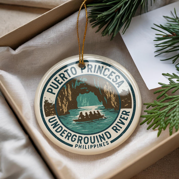 A round ornament with a design depicting a boat on a river, surrounded by lush greenery, with the text "PUERTO PRINCESA UNDERGROUND RIVER PHILLIPPINES" printed on it.