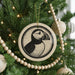 A Christmas tree decorated with ornaments, including a circular ornament featuring a black and white illustration of a puffin bird.