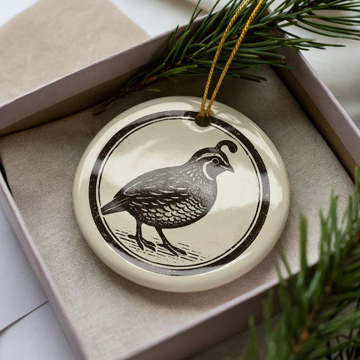A ceramic ornament in the shape of a bird, possibly a quail, is displayed in a box with pine branches.