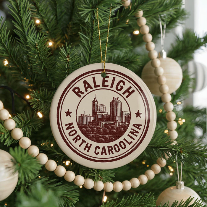 A Christmas tree decorated with ornaments, including a circular ornament with the text "RALEIGH NORTH CAROLINA" and a cityscape illustration.