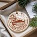 A circular ornament with the text "RAROTONGA COOK ISLANDS" printed on it, surrounded by a string and placed on a white cloth with pine branches.
