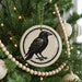 A black and white ceramic ornament featuring a bird is hanging on a Christmas tree, surrounded by ornaments and lights.