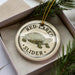 A round ornament with a turtle image and the text "RED-EARED SLIDER" on it, placed in a box with pine branches.
