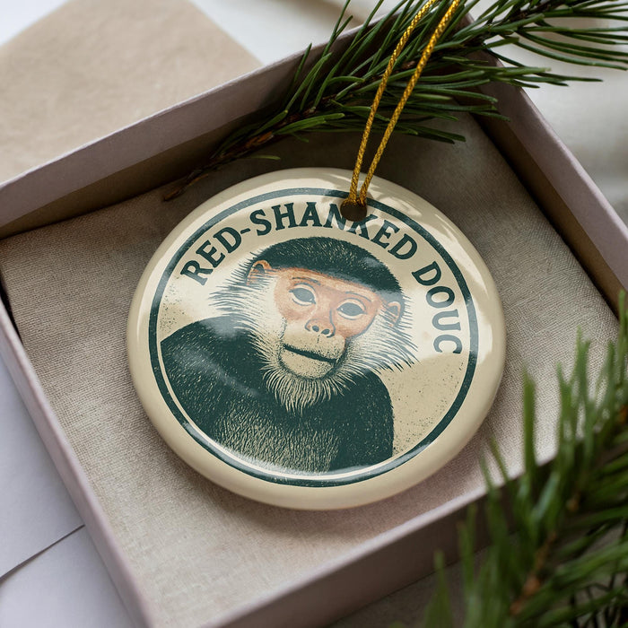 A round ornament with a monkey image and the text "RED-SHANKED DOUC" is displayed in a box, surrounded by pine branches.