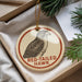 A round ornament with a bird illustration and the text "RED-TAILED HAWK" on it, placed in a box with pine branches.