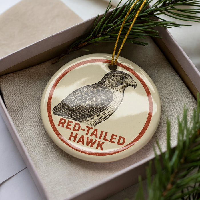 A circular ornament with a red border and a black and white illustration of a red-tailed hawk.