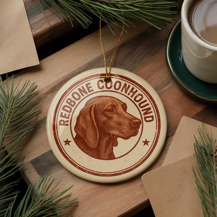 A circular ornament featuring a brown dog's head, with the text "REDBONE COONHOUND" around the edge, placed on a wooden surface next to a cup of coffee and pine branches.