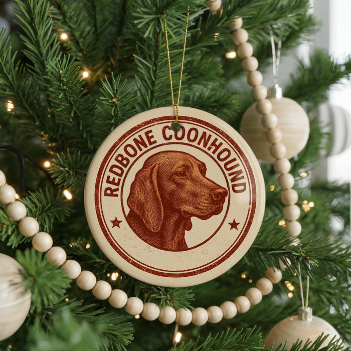 A Christmas tree decorated with ornaments, including a circular ornament with a red and brown image of a redbone coonhound and the text "REDBONE COONHOUND" on it.