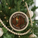 A Christmas tree decorated with ornaments, including a circular ornament with the text "REDWOOD NATIONAL PARK USA" and a tree with white beads.