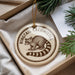 A round ornament with a raccoon image and the text "Ringtail Cacomistle" is displayed in a box with pine branches.