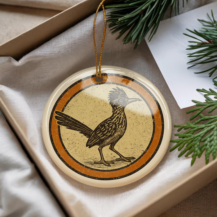 A decorative ornament featuring a bird, likely a roadrunner, is displayed in a box with pine branches.