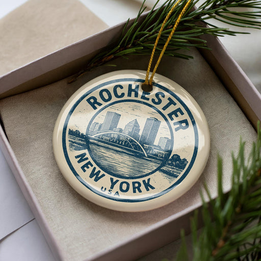 A decorative ornament in a box, featuring a circular design with a cityscape and the text "Rochester, New York" printed on it.