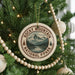A Christmas tree decorated with ornaments, including a circular ornament with a mountain landscape and text, surrounded by lights and greenery.