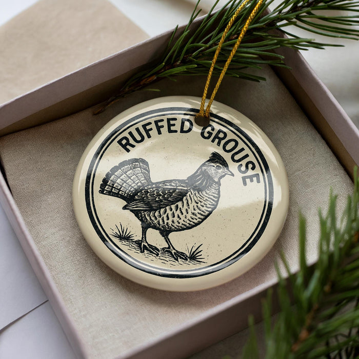 A decorative ornament in a box, featuring a black and white illustration of a bird and the text "RUFFED GROUSE" around the edge.