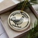 A decorative ornament in a box, featuring a black and white illustration of a bird and the text "RUFFED GROUSE" around the edge.