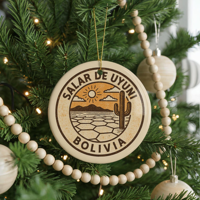 A round ornament on a Christmas tree, featuring a desert landscape with a cactus and mountains, along with the text "Salar de Uyuni Bolivia".