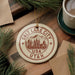 A circular ornament with the text "Salt Lake City USA Utah" printed on it, surrounded by pine branches and a cup of coffee on a wooden surface.