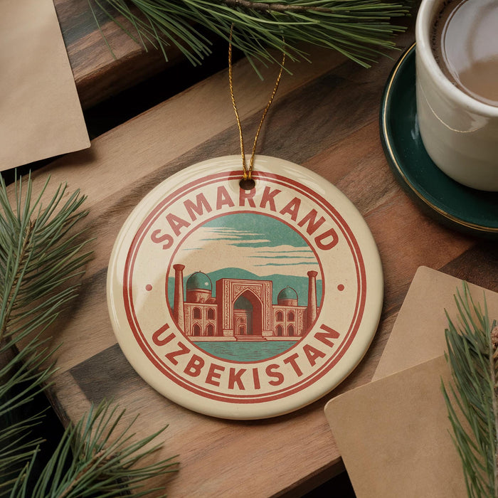 A circular ornament with the text "SAMARKAND UZBEKISTAN" and an illustration of a building, placed on a wooden surface next to a cup of coffee and some pine branches.