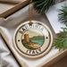 A decorative ornament with the text "SARDINIA ITALY" and a scenic illustration of a coastal town, surrounded by pine branches.