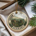 A round ornament with a scenic mountain landscape and the text "SAXON SWITZERLAND GERMANY" printed on it, hanging from a string.
