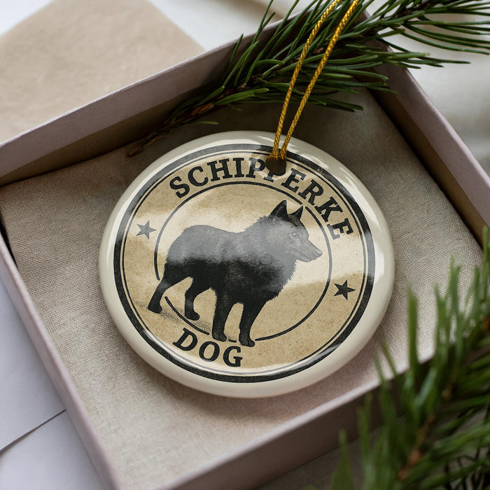 A round ornament with a black silhouette of a dog and the text "SCHIPERKE DOG" printed on it, hanging from a string.