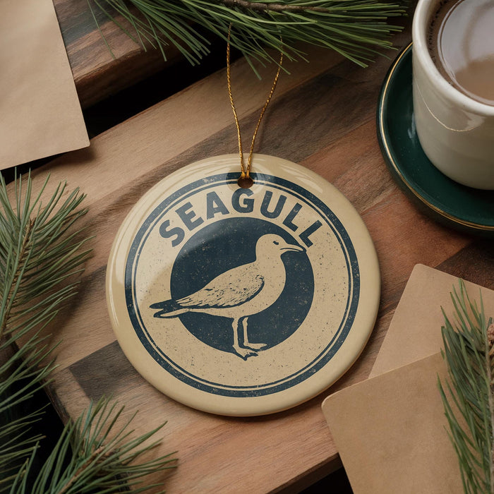 A decorative ornament featuring a seagull is displayed on a wooden surface, accompanied by a cup of coffee and pine branches.