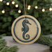 A round ornament featuring a seahorse design is displayed against a blurred background of a Christmas tree with twinkling lights.