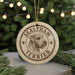 A round ornament featuring a terrier dog's head, with the text "SEALYHAM TERRIER" printed on it, hanging in front of a Christmas tree with twinkling lights.