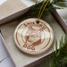 A circular ornament with a dog image and the text "SHIKOKU DOG" printed on it, placed inside a box with pine branches.