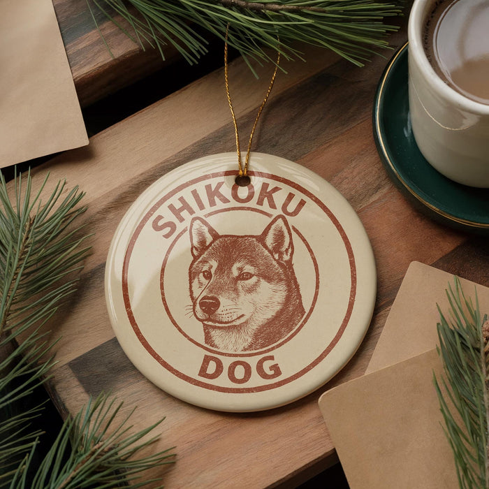 A round ornament with a dog image and the text "SHIKOKU DOG" is displayed on a wooden surface, surrounded by pine branches and a cup of coffee.
