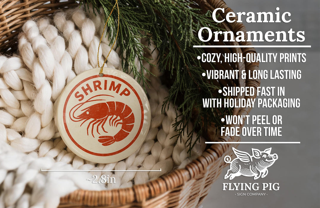Ceramic ornaments, including a shrimp ornaments, are displayed in a basket with a pine branch.