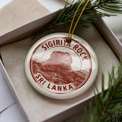 A decorative ornament featuring the Sigsiriya Rock, a famous landmark in Sri Lanka, is displayed in a box with pine branches.