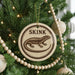 A Christmas tree decorated with ornaments, including a round ornament with a lizard image and the word "SKINK" written on it.