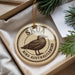 A circular ornament with a bird image and text, placed on a surface with pine branches and a white paper.