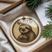 A round ornament featuring a smiling sloth, with the word "SLOTH" written on it, is displayed in a box with pine branches.