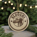 A circular ornament with the word "SLOUGHI" and a dog's head image, hanging from a string against a background of Christmas lights and greenery.