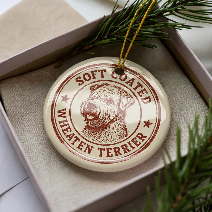 A circular ornament with a dog image and the text "Soft Coated Wheaten Terrier" printed on it, placed inside a box with pine branches.