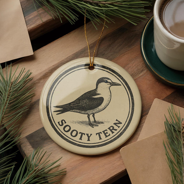 A round ornament featuring a bird, specifically a seagull, is displayed on a wooden surface alongside a cup of coffee and some pine branches.